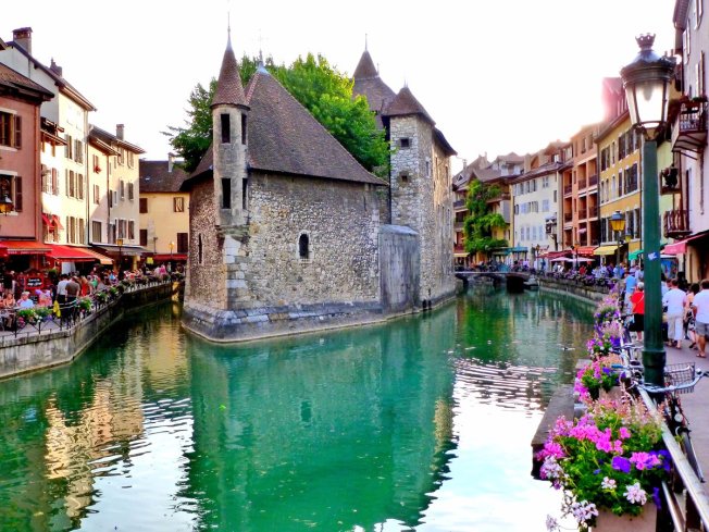 in-the-old-town-of-annecy-france-travelers-are-greeted-by-pastel-painted-houses-and-cafes-lining-a-lovely-lakeshore-hang-out-at-one-of-its-many-outdoor-eateries-cycle-along-the-_png